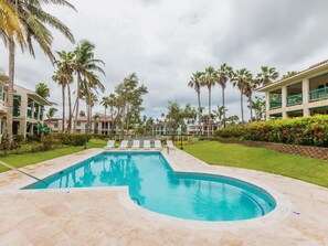 A swimming pool surrounded by palm trees and a building with multiple balconies.