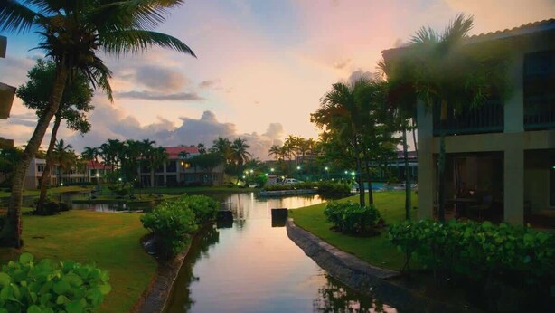 A serene waterway with a bridge, palm trees, and buildings in the background. - Giovanni Beachfront community w/pools (Sabana)