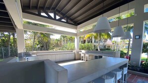 A covered outdoor bar area with a long counter, white bar stools, and hanging pendant lights. - Giovanni Beachfront community w/pools (Sabana)