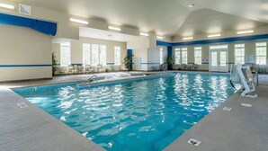An indoor swimming pool with clear blue water, surrounded by lounge chairs and tables.