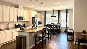 A modern kitchen with white cabinets, a central island, and bar stools.