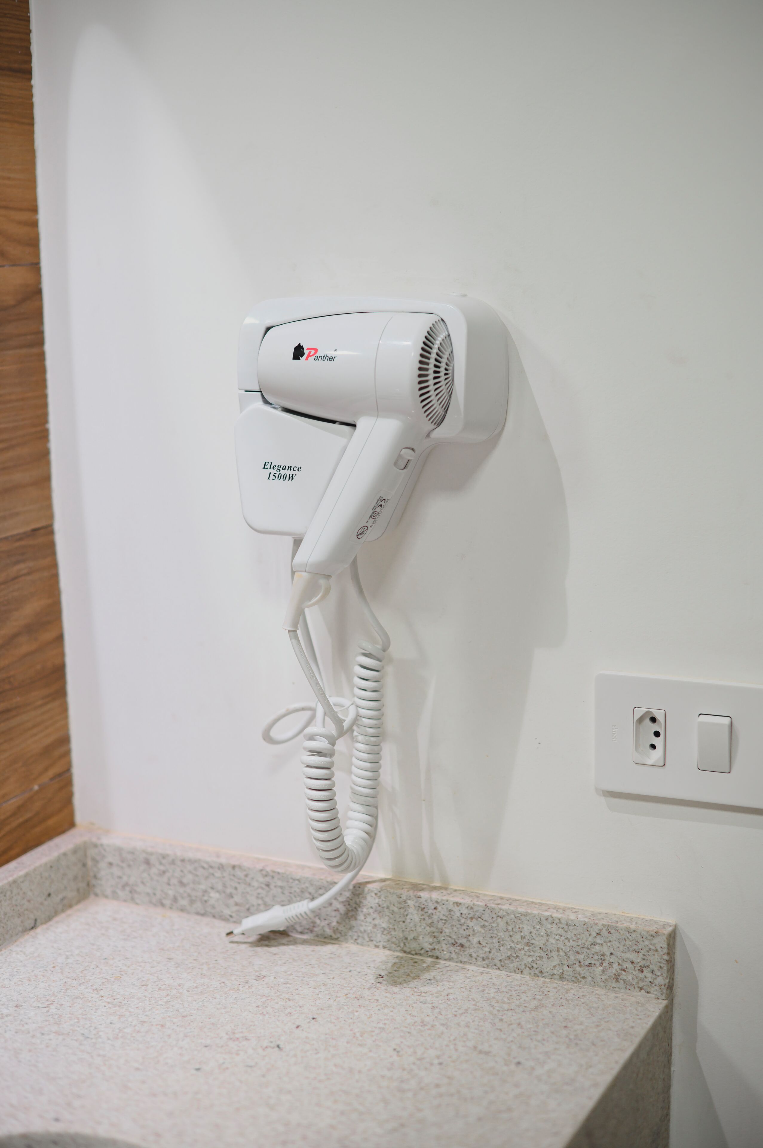 Un sèche-cheveux blanc fixé au mur, à côté d’une prise de courant.