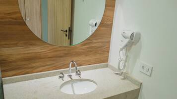 Un baño con tocador de madera, un espejo redondo, un lavamanos blanco y un secador de pelo en la pared.