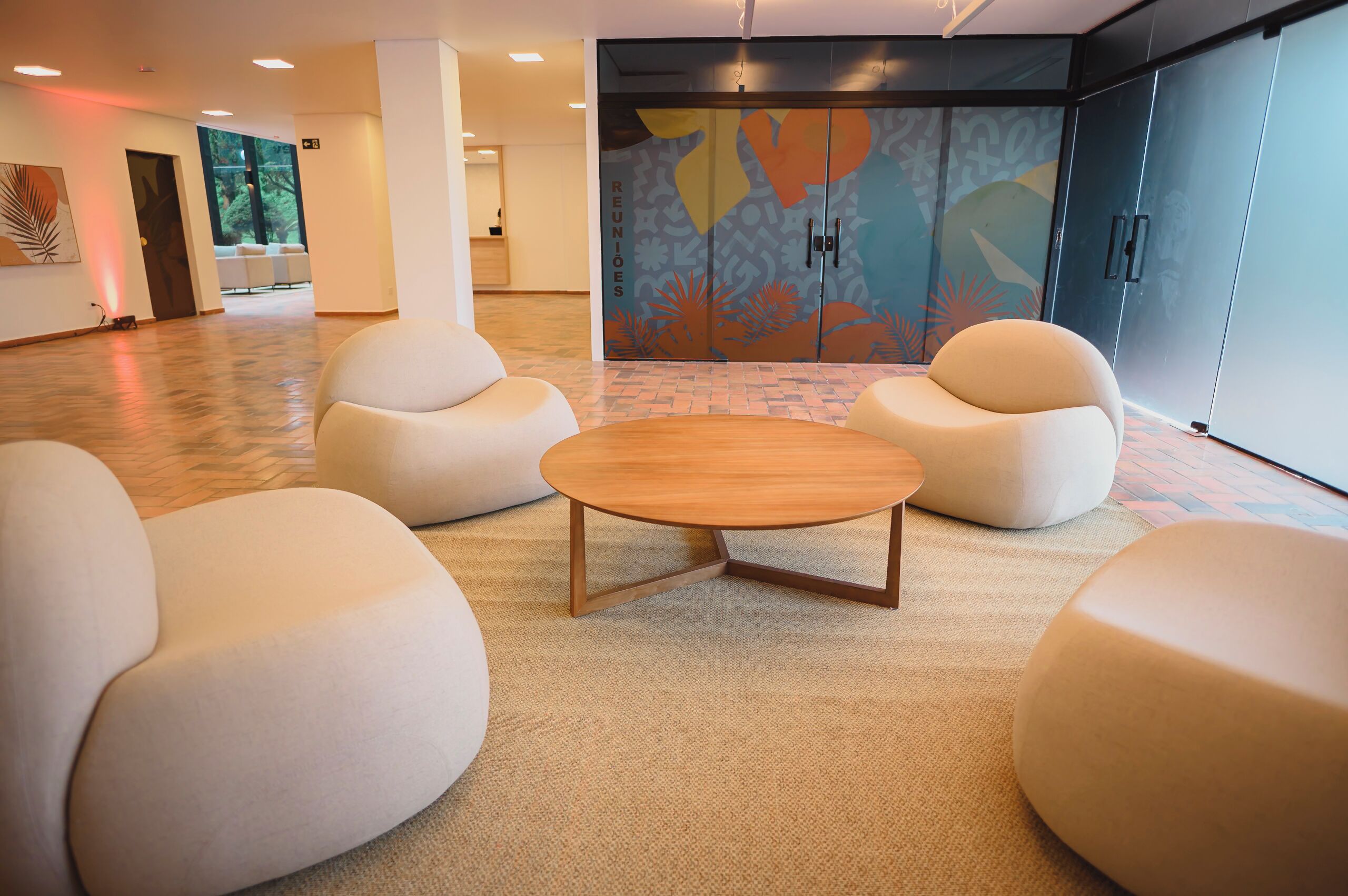 Un área de descanso moderna con una mesa redonda de madera y cuatro sillones beige.