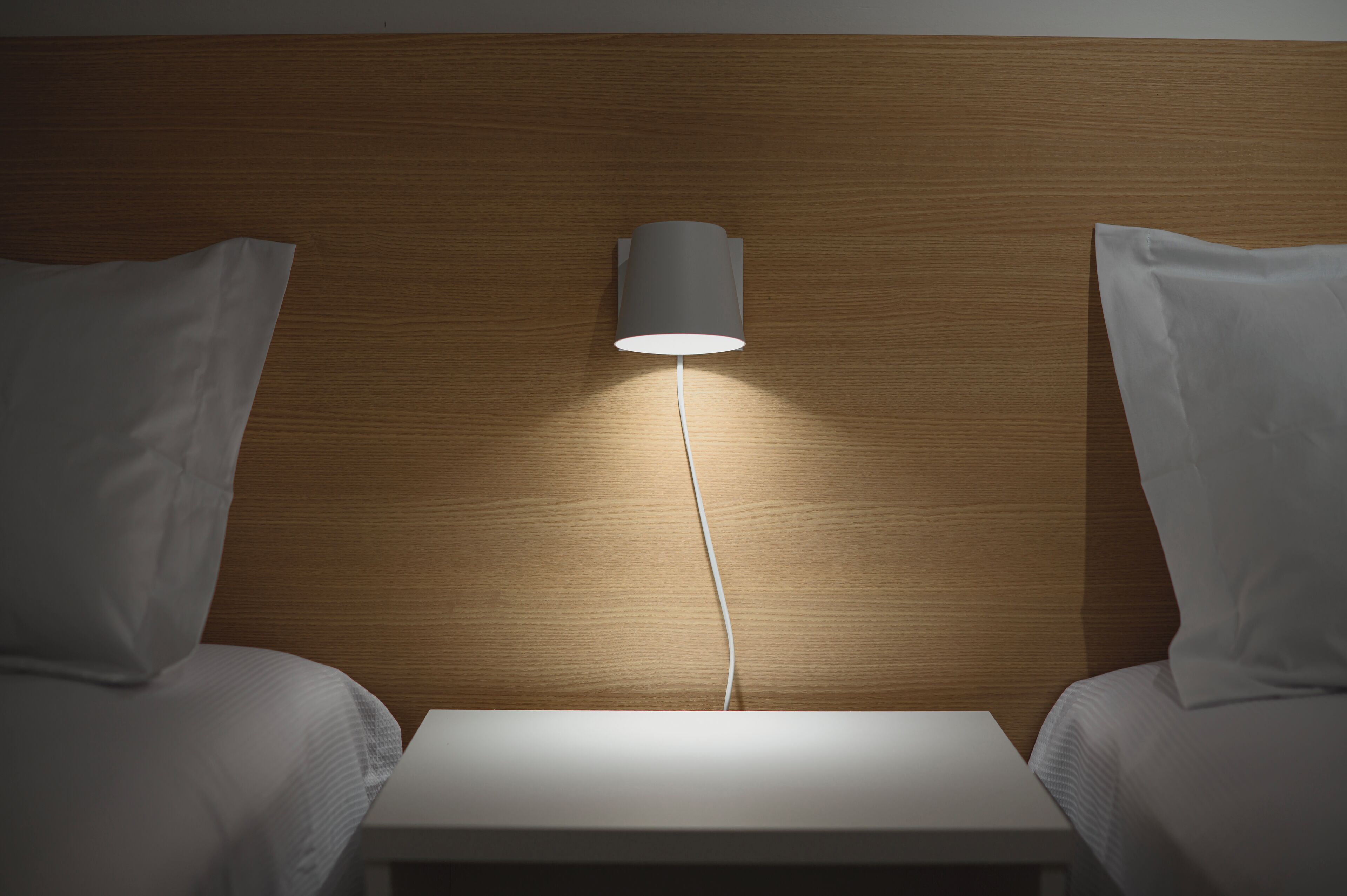 A hotel room with a wooden headboard, a bedside table, and two white pillows.