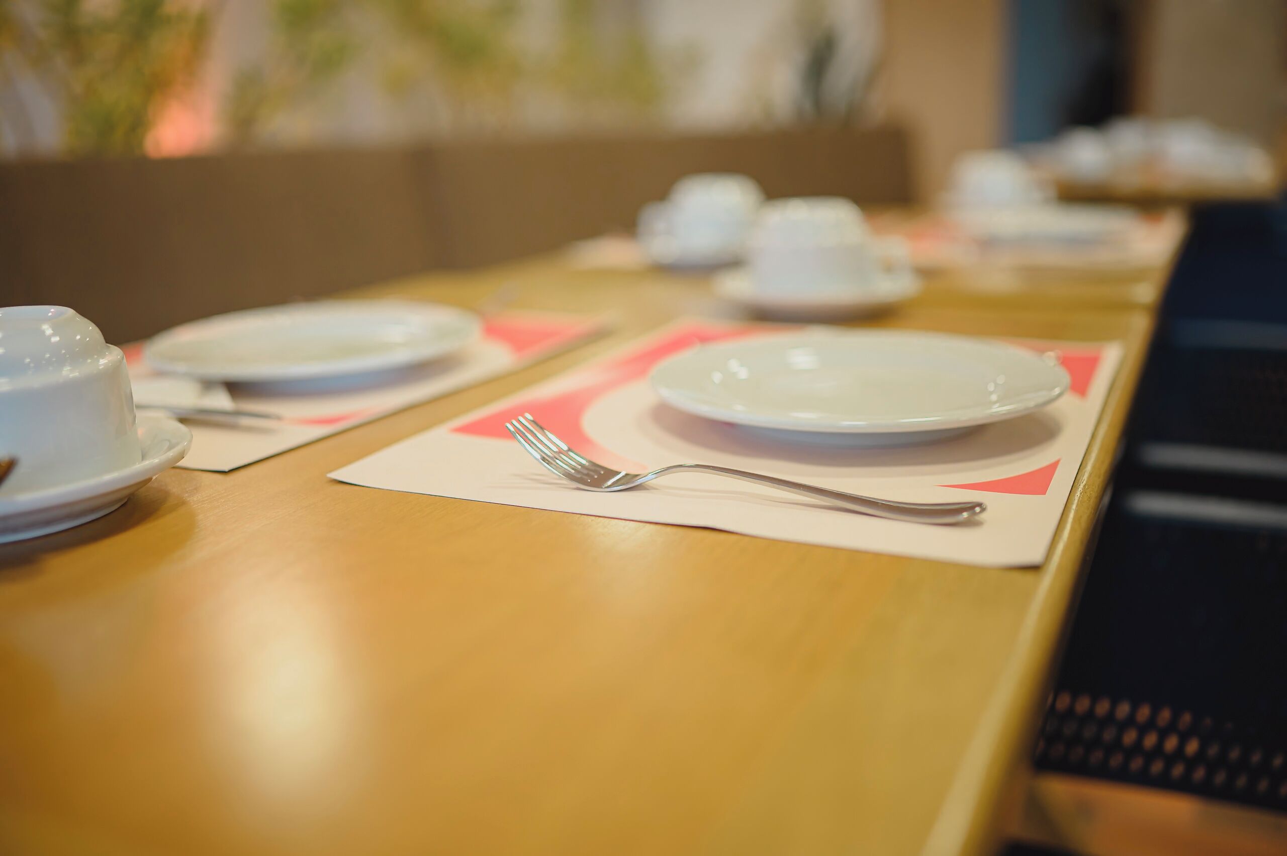 Mesa de jantar com pratos brancos, garfos de prata e jogos americanos cor-de-rosa.