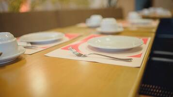 Mesa de jantar com pratos brancos, garfos de prata e jogos americanos cor-de-rosa.