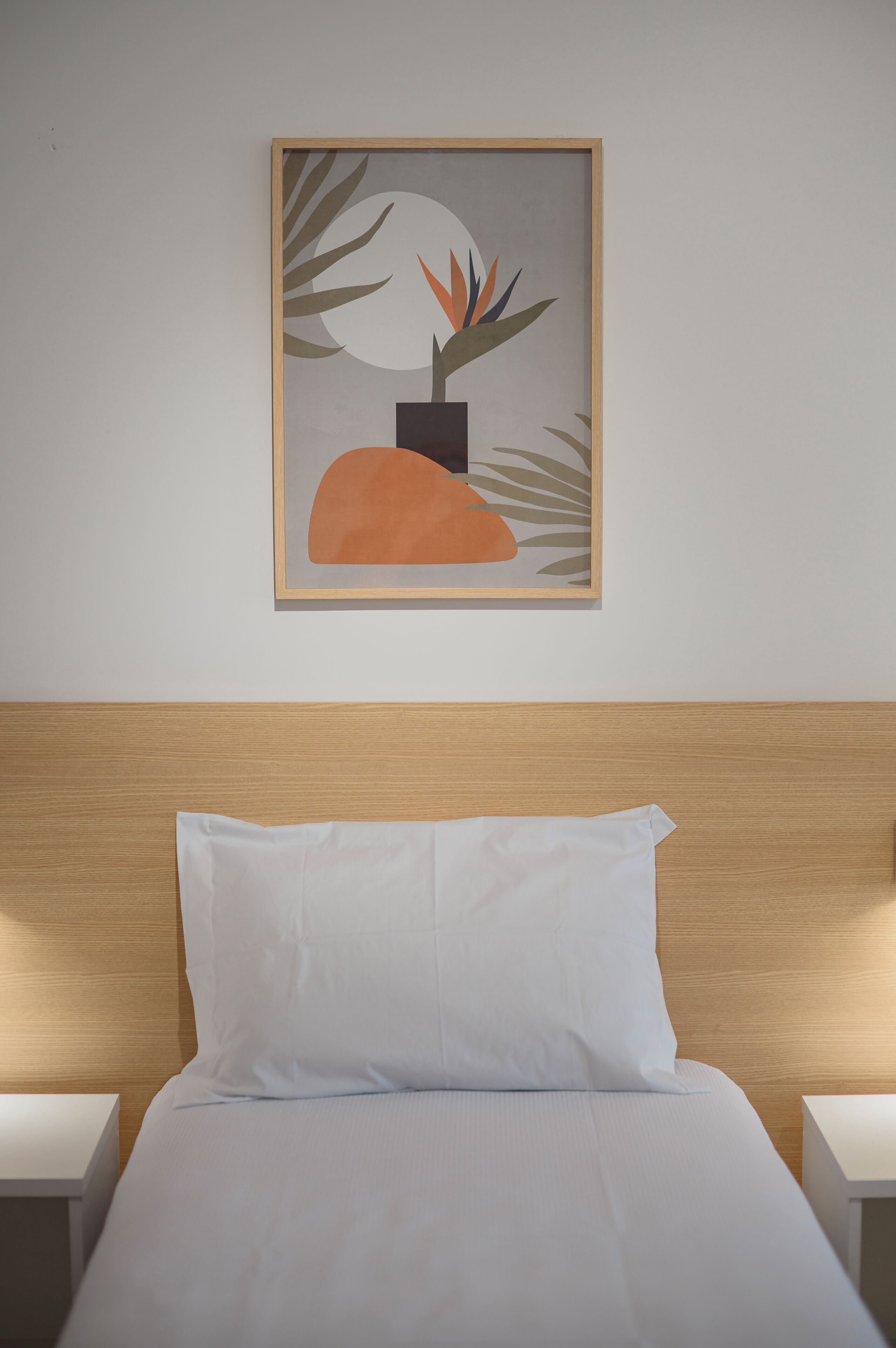 Una cama bien hecha con ropa blanca, un cabecero de madera y una obra de arte abstracta enmarcada en la pared de arriba.