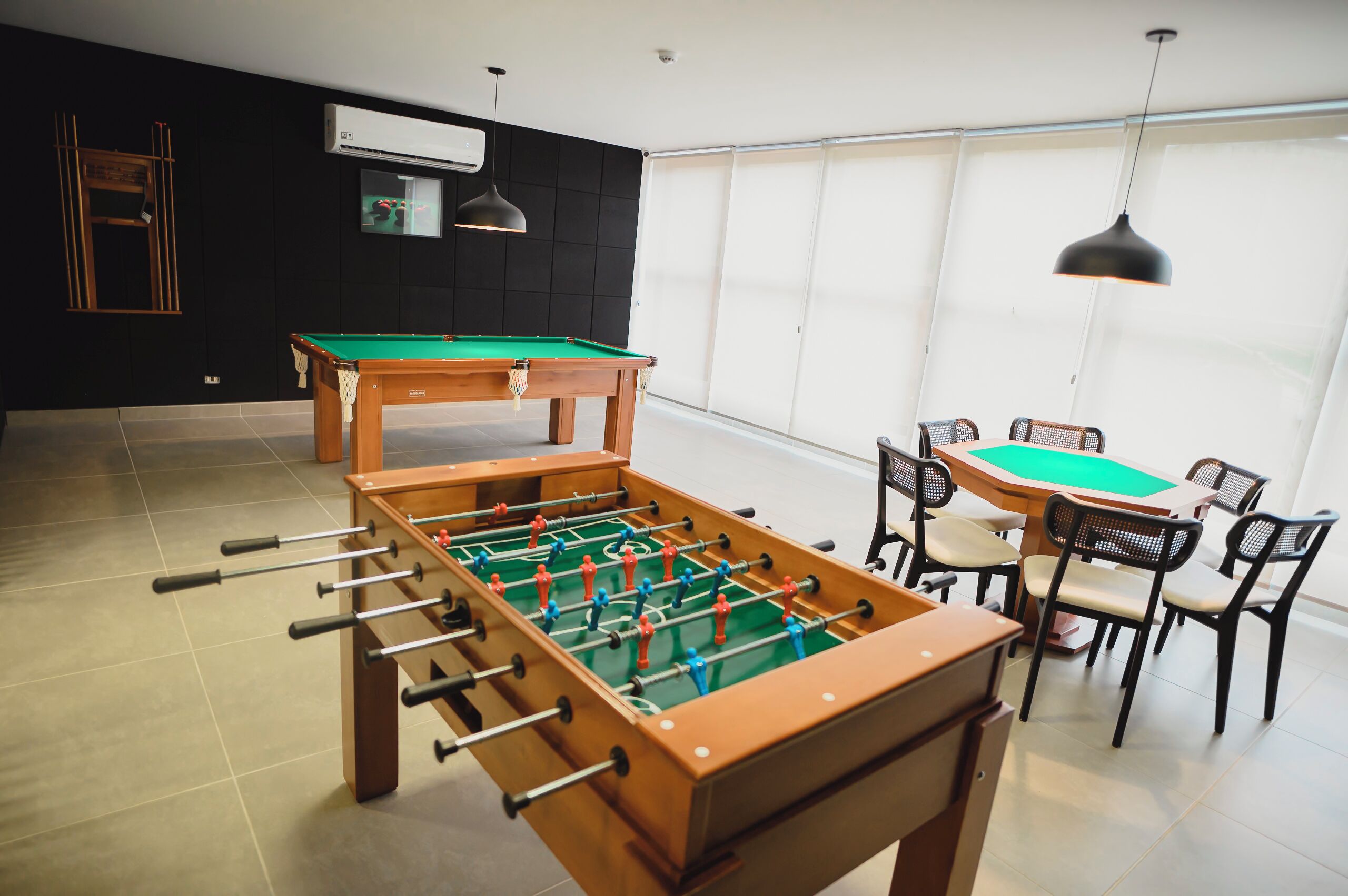 Een kamer met een tafelvoetbaltafel, een pooltafel en een biljarttafel. Er staan vier stoelen bij de tafels.