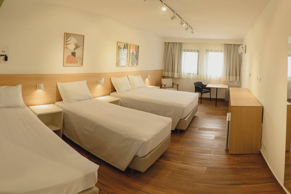 Ein Hotelzimmer mit drei Einzelbetten, einem Schreibtisch und einem Stuhl.