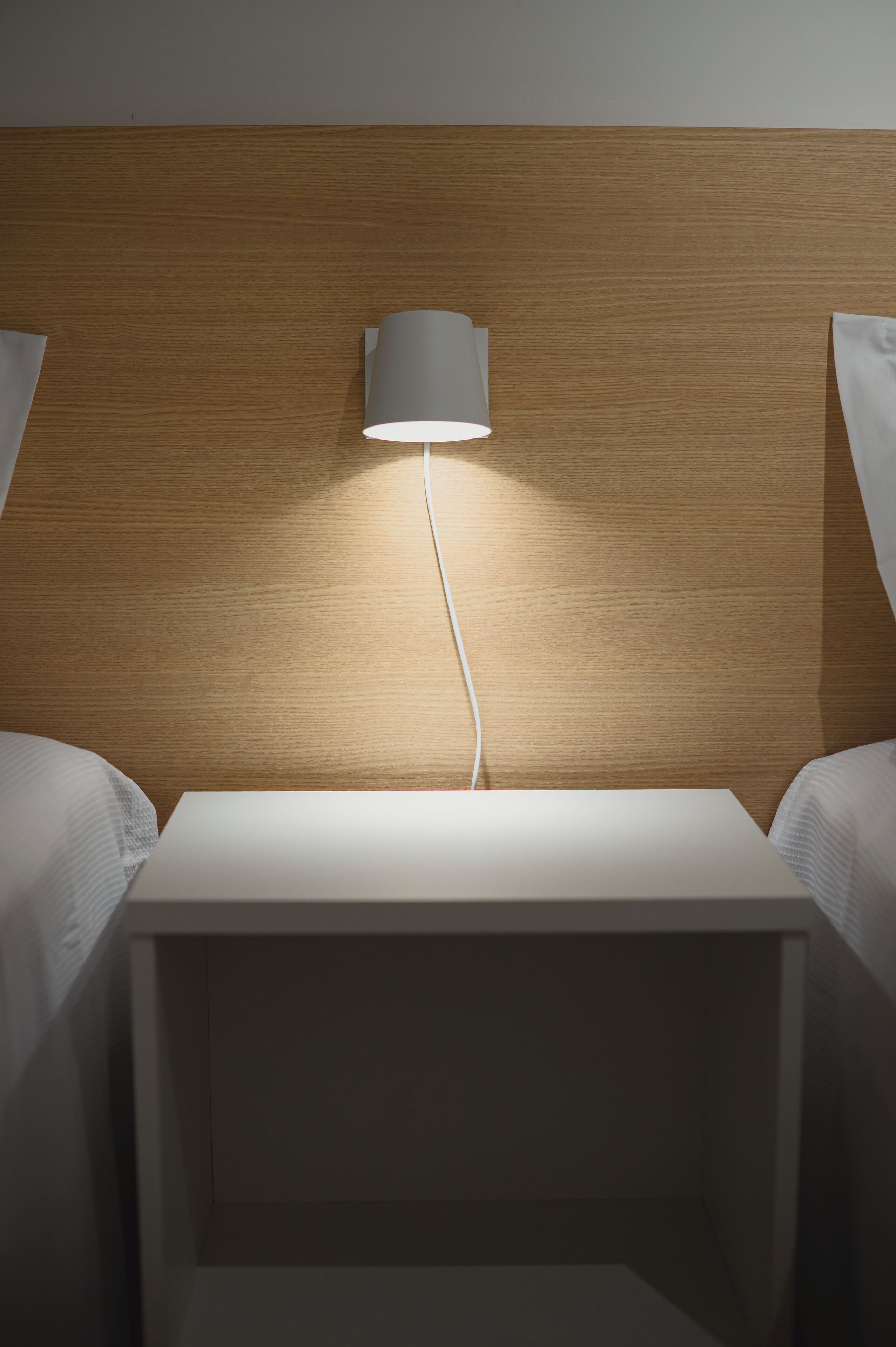 Une chambre d’hôtel avec une tête de lit en bois, une table de chevet et une lampe.