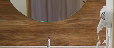 A bathroom with a round mirror, a sink, a faucet, a hairdryer, and a light fixture.