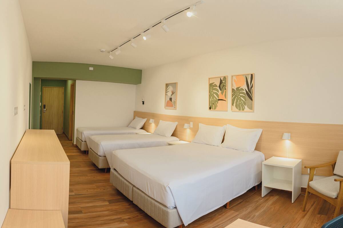 Ein Hotelzimmer mit drei Betten, Holzboden, einem Schreibtisch und einem Stuhl.