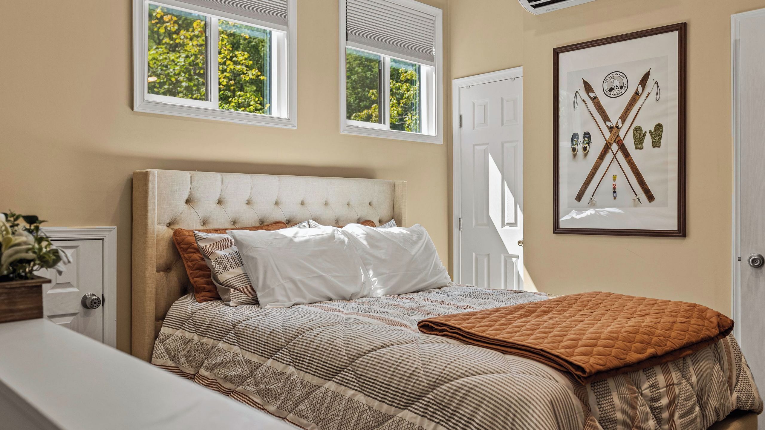 A bedroom with a tufted headboard, a bed with patterned bedding, a quilted throw blanket, and a framed picture on the wall.