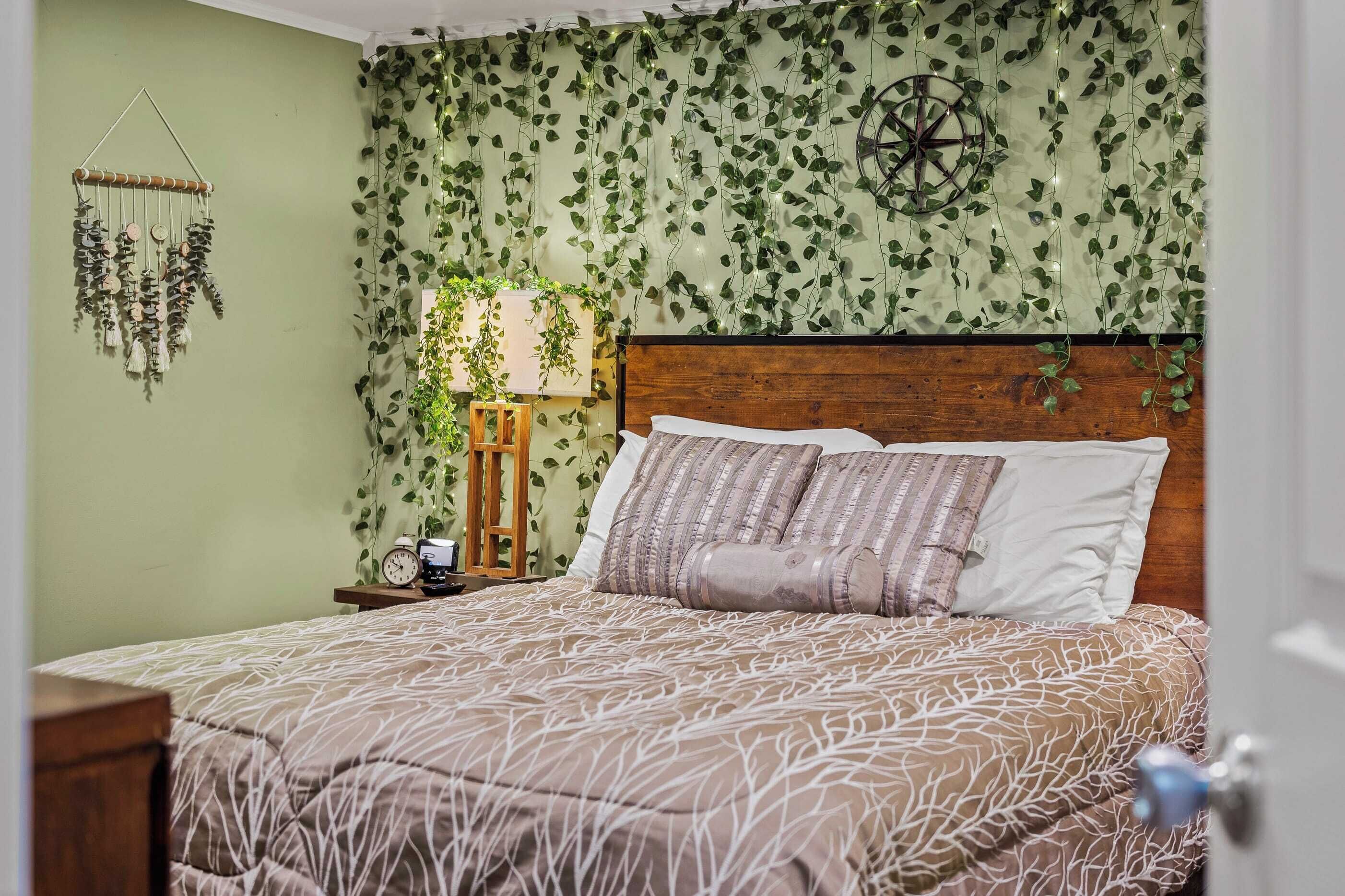 A bedroom with a bed, a wooden headboard, a wall clock, a hanging plant, and a wall-mounted wind chime.