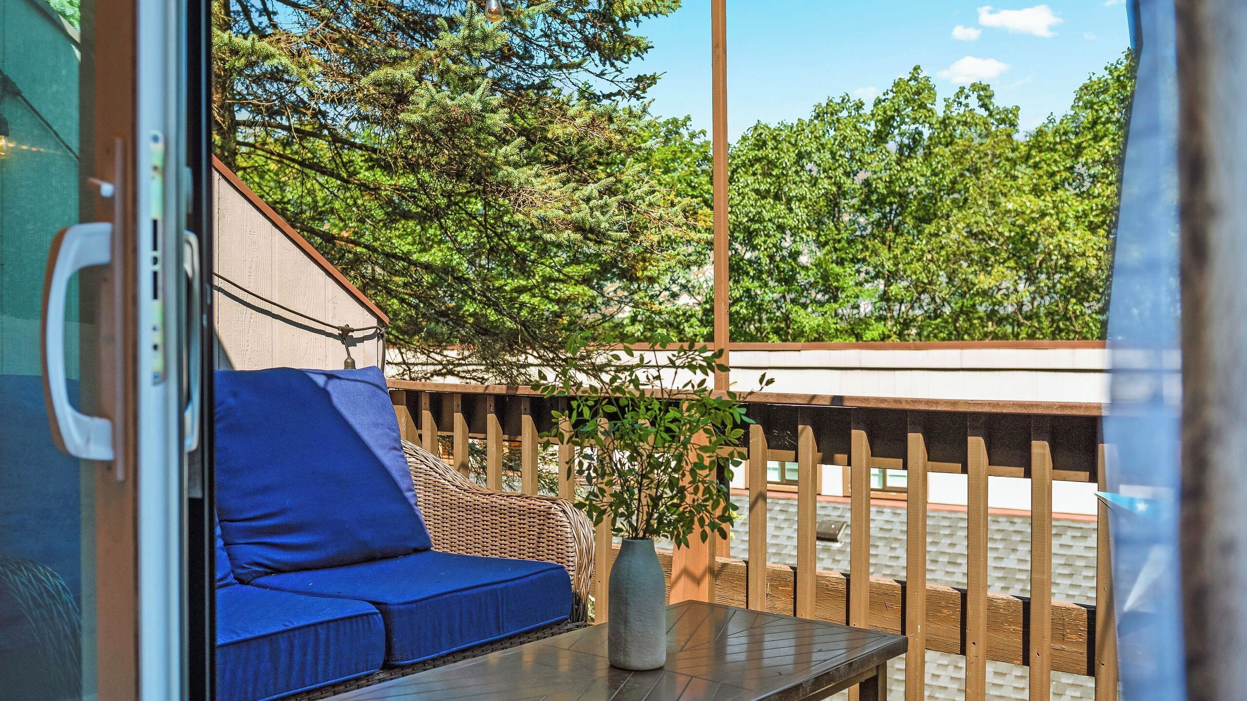 A balcony with a wicker sofa, a table, and a potted plant.