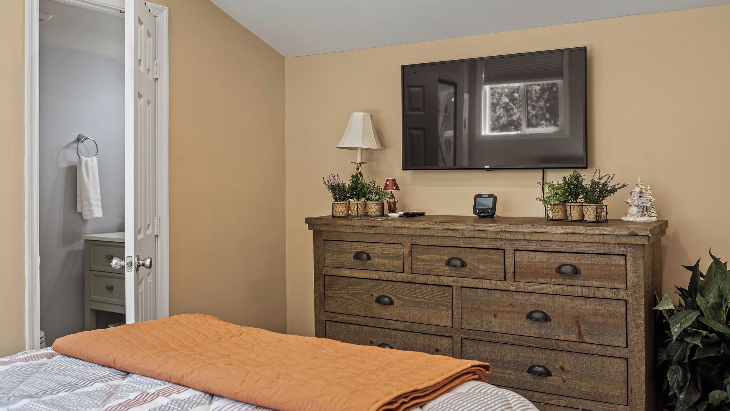 A bedroom with a bed, dresser, TV, and a door leading to a bathroom.