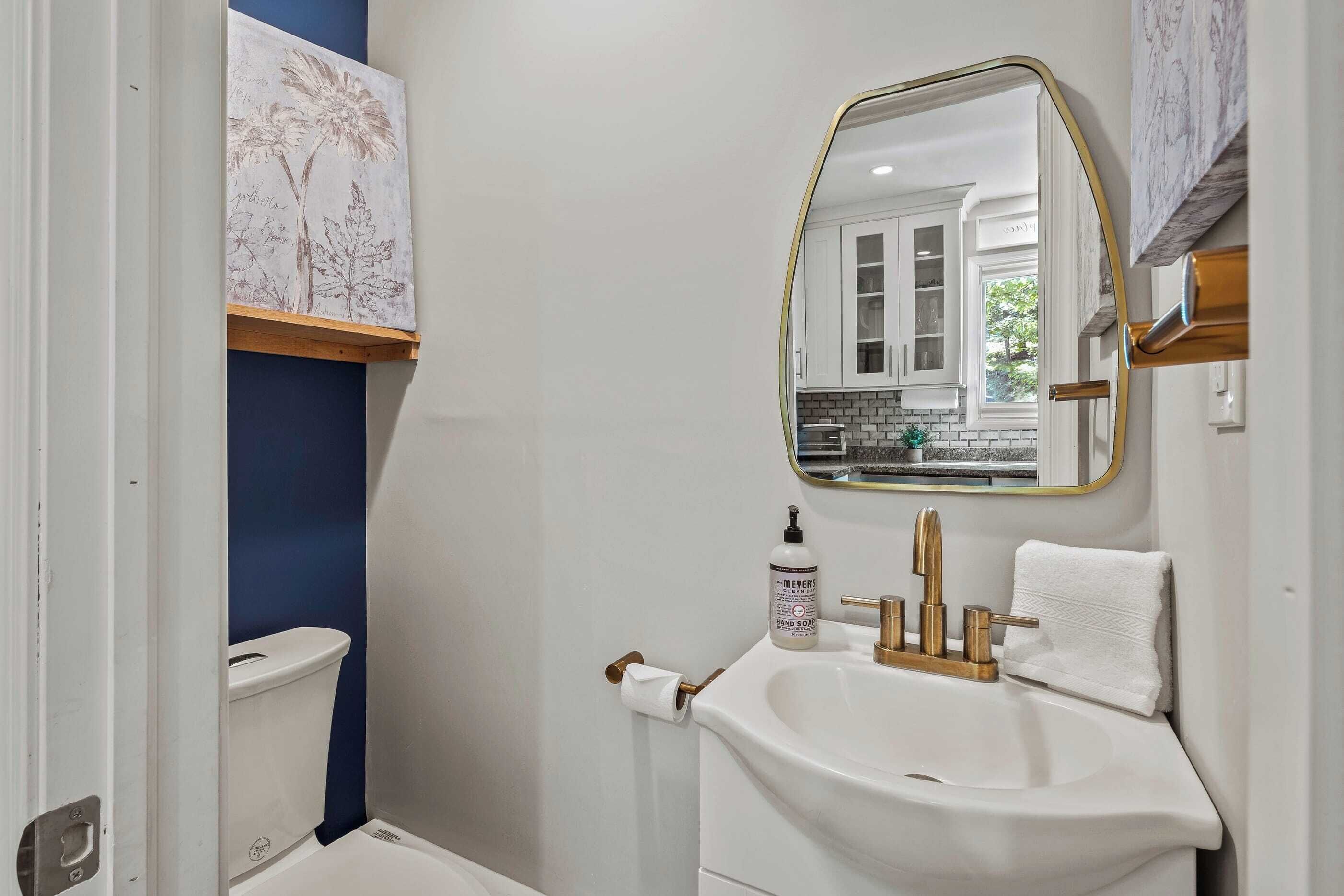 A bathroom with a white sink, gold faucet, and a mirror with a gold frame.