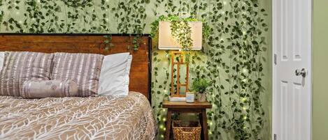 A bedroom with a bed, a bedside table with a lamp, and a wall covered in green ivy.
