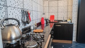 A modern kitchen with a gas stove, a kettle, and various utensils hanging on the wall.