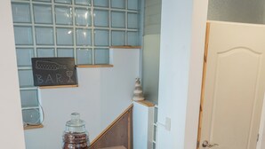 A small kitchen area with a wooden counter, a stool, and a glass jar of spices.
