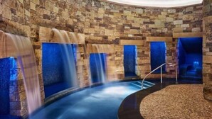 Een wellnessruimte met stenen muren, een rond bubbelbad en verschillende waterpartijen.
