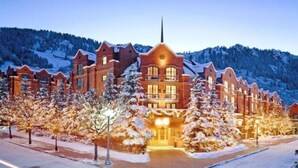 Un gran hotel de varios pisos con una fachada simétrica, árboles cubiertos de nieve y un telón de fondo montañoso.
