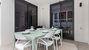 Enjoy meals in this dining area with a glass table and four chairs, surrounded by large glass doors leading to an outdoor space.