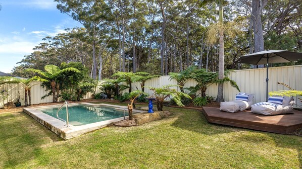 A backyard with a swimming pool, a deck with lounge chairs, and a variety of trees and shrubs.