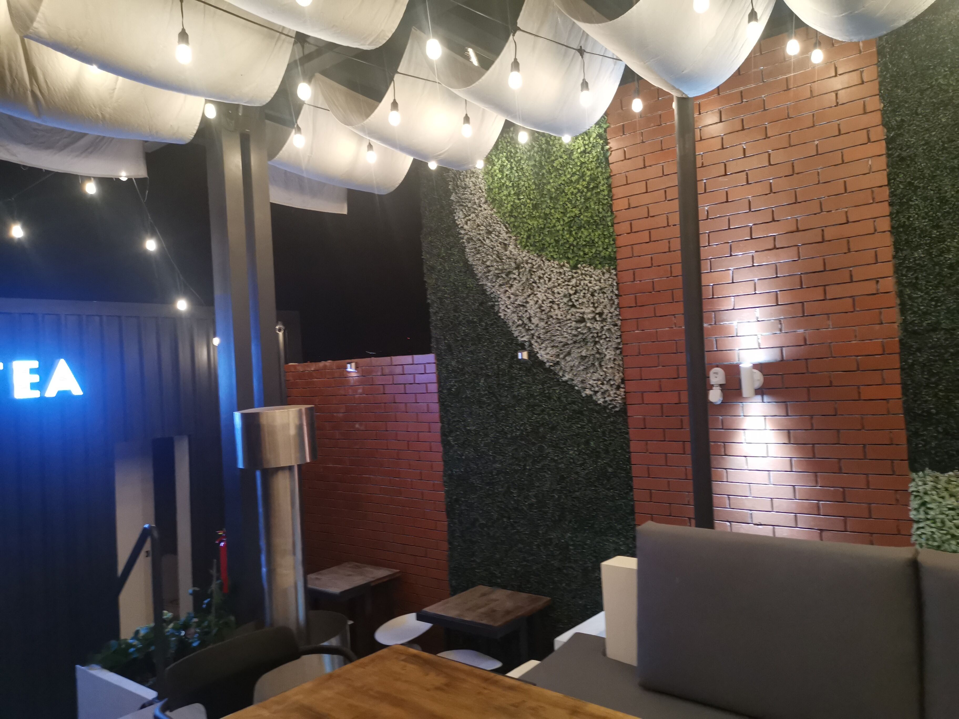 A restaurant interior with a brick wall, green foliage wall, and hanging lights.