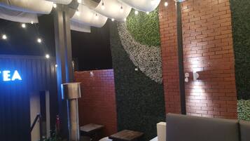 A restaurant interior with a brick wall, green foliage wall, and hanging lights.