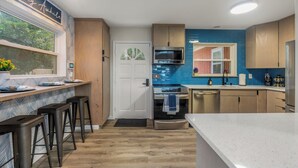 A modern kitchen with a bar area, wooden cabinets, a stainless steel oven, and a blue backsplash. - The Dock House (Savannah)