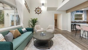 A spacious living area with a green sofa, two armchairs, a round coffee table, and a view of a kitchen and staircase. - The Dock House (Savannah)