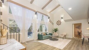 A spacious living area with a green sofa, a round coffee table, and a white rug. There is a staircase with a wooden railing leading to another level. - The Dock House (Savannah)