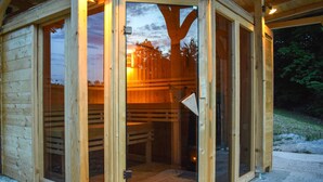 A wooden cabin with a glass door, a wooden deck, and a view of trees.