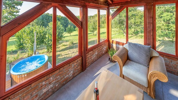 A wooden deck with a hot tub, a wicker sofa, and a table with wine glasses and a bottle.