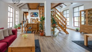 A spacious living room with a wooden staircase, a red sofa, a coffee table, and a bookshelf filled with books and decorative items.