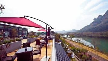 Terraza al aire libre con asientos y sombrillas con vistas a un río y montañas.