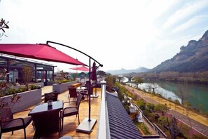 Terraza al aire libre con asientos y sombrillas con vistas a un río y montañas.