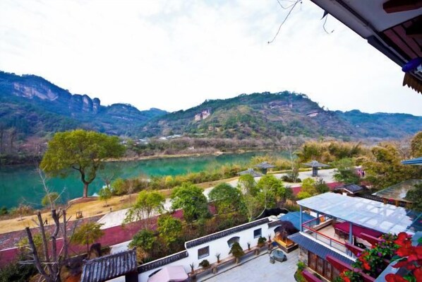 A view of a mountainous landscape with a river, buildings with traditional architecture, and a balcony with red flowers.