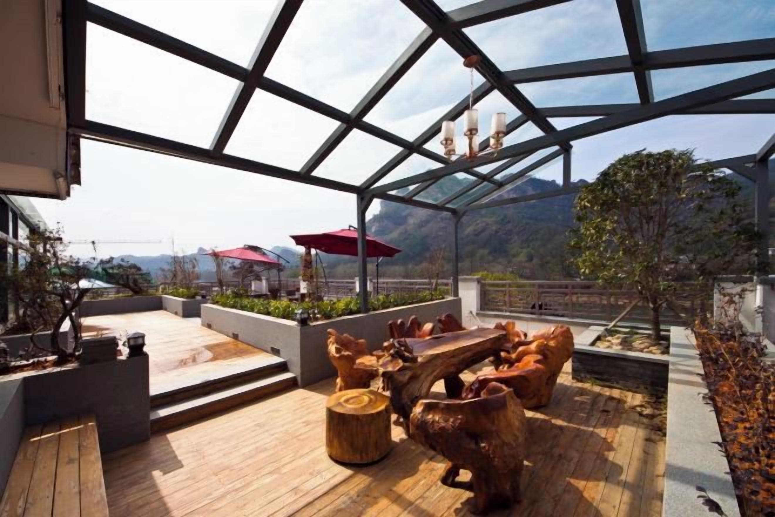 An outdoor terrace with wooden furniture, a glass roof, and a view of mountains.
