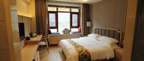A hotel room with a large bed, a desk with a chair, a window with curtains, and a television on the left side.