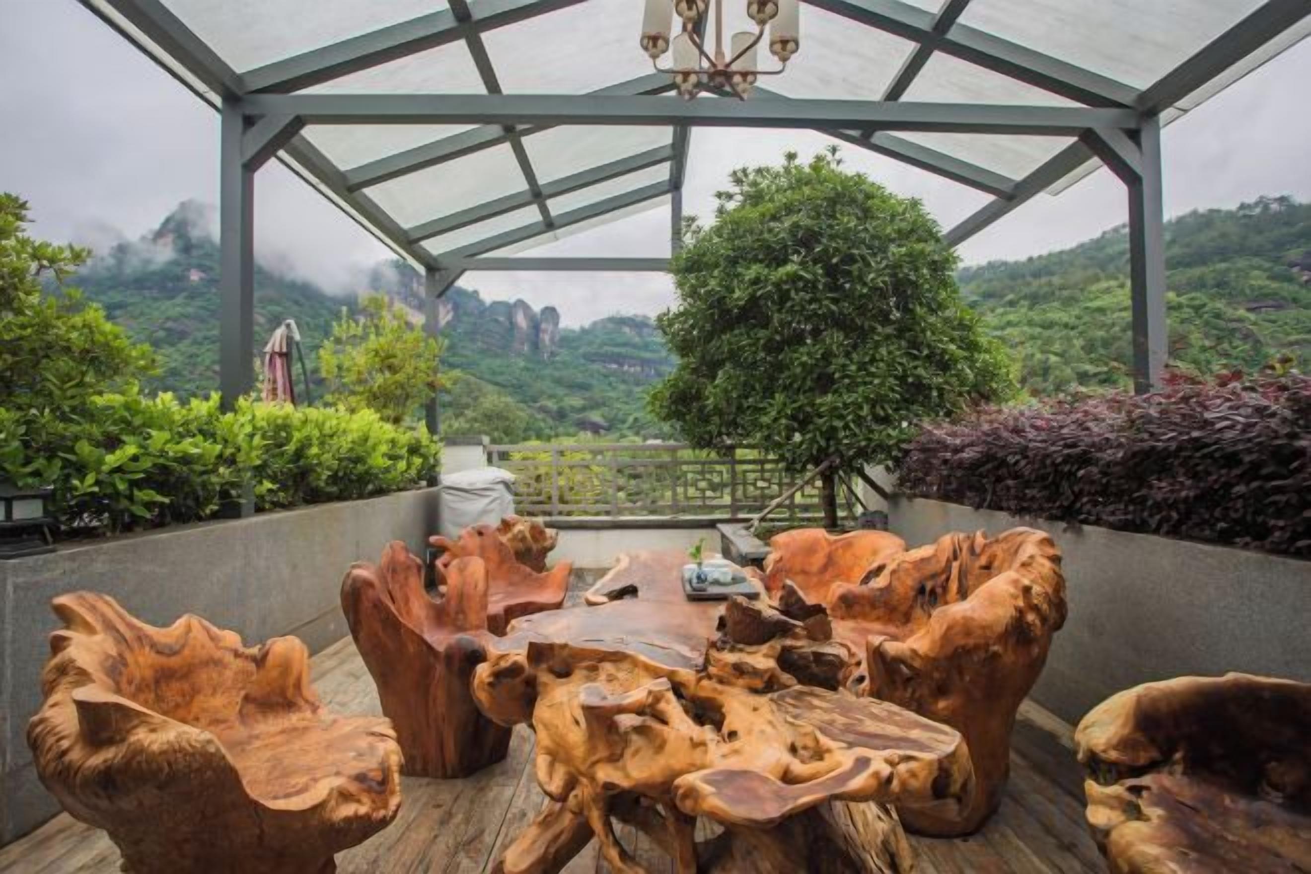 A covered outdoor seating area with a table and chairs made of natural wood, overlooking a mountainous landscape.