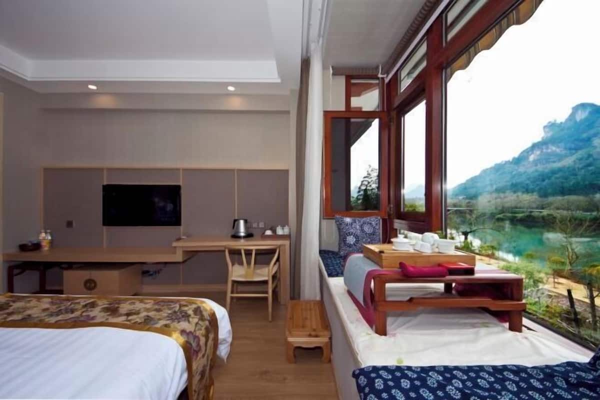 A hotel room with a bed, a desk, a television, and a window with a mountain view.