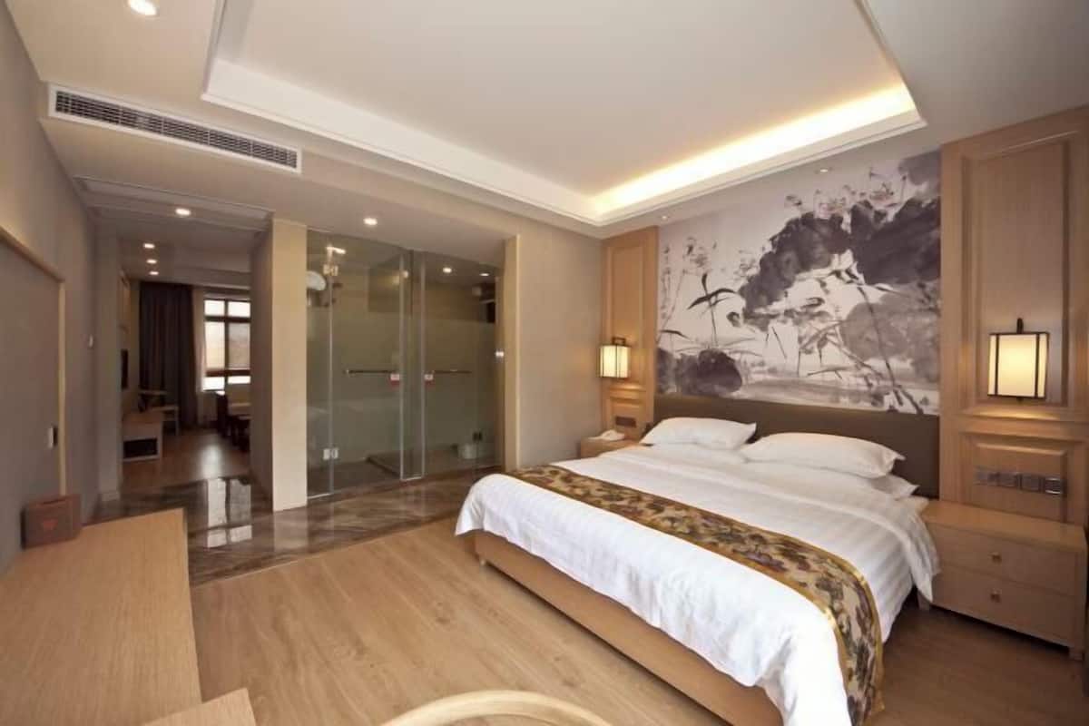 A hotel room with a large bed, a desk, a glass shower, and a mural on the wall.
