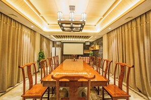 Une salle de conférence avec une longue table en bois et des chaises, un écran de projection et un lustre moderne.