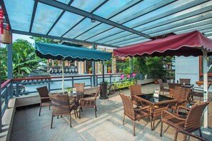 Un espace extérieur aménagé en terrasse, avec des meubles en osier, une balustrade en verre et des plantes en pot.