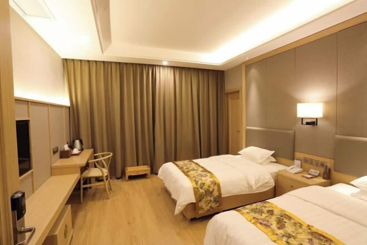 A hotel room with two beds, a desk, a chair, a nightstand, and a lamp.