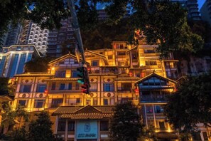 A multi-story building with traditional architectural design, illuminated by warm lighting, surrounded by trees.