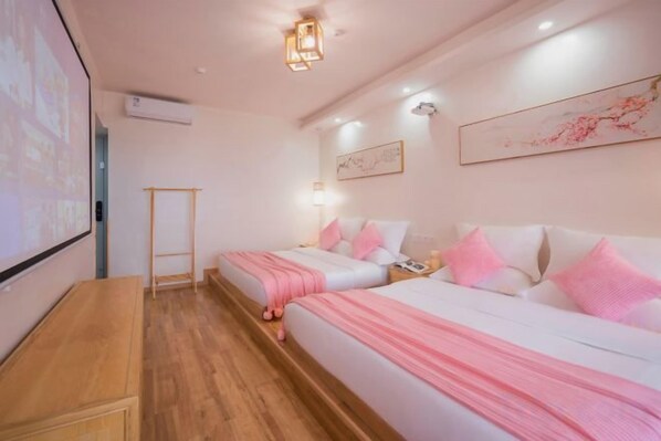 A hotel room with two beds, a wooden desk, a projector screen, and a wall-mounted artwork.